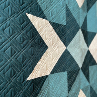Close-up view of a geometric quilt with cream and teal shapes showcasing intricate quilting detail, featured in the Mt. Mitchell Quilt Pattern (Download) by Hampton Quilt Studio.