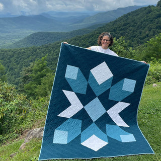 Mt. Mitchell Quilt Pattern by Hampton Quilt Studio cover: woman holding a navy, teal, and white geometric star quilt with 3D diamond blocks against a mountain backdrop.