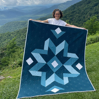 Mt. Pisgah Quilt Pattern by Hampton Quilt Studio cover: person holding a teal and navy large star-block quilt in front of a lush green mountain view.