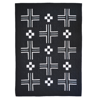 Mudroom Quilt Pattern by Sewn cover flat lay: bold black quilt with repeating white cross and pinwheel block shapes, photographed on a white background.