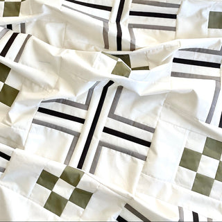 Close-up of a modern quilt in olive green, black, and gray tones, featuring geometric blocks made with the Mudroom Quilt Pattern (Download) by Sewn.