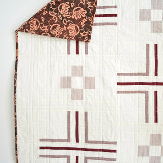 Close-up of a modern quilt with simple geometric shapes in soft gray and burgundy tones, featuring a floral patterned backing, showcasing Sewn's Mudroom Quilt Pattern (Download).