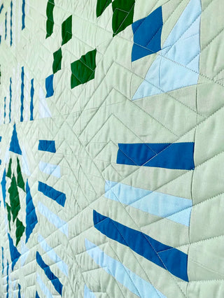 Quilt with geometric pattern in blue, green, and beige on a white background