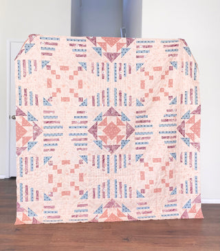 Quilt with geometric pattern draped over a chair in a room.