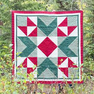 Cozy quilt with geometric star and flying geese blocks in red, green, and white, made using Northern Glow Quilt Pattern (Download) by Shadow Valley Quilts.