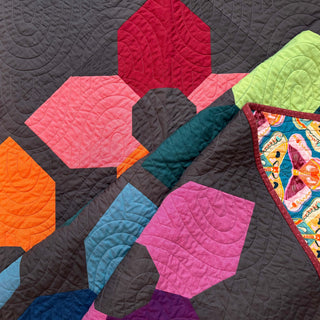 Close-up of a colorful geometric quilt featuring floral-inspired shapes and intricate curved quilting, showcasing the Orchid Garden Quilt Pattern (Download) by A Piece of Quiet Quilts.