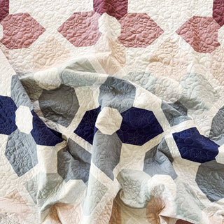 Close-up of a softly folded quilt with geometric flower patterns in muted blues and pinks, showcasing intricate stitching from A Piece of Quiet Quilts using the Orchid Garden Quilt Pattern (Download).