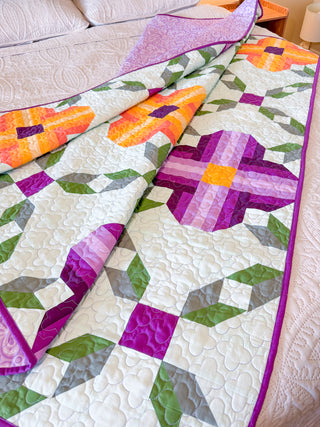 Close-up of colorful floral quilt with purple, orange, and green patterns, laid on a bed, showcasing Pansy Picnic Quilt Pattern (Download) by Shadow Valley Quilts.