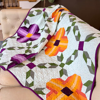 A colorful floral quilt with orange and purple pansy designs, green leaf details, and a purple border, showcasing the Pansy Picnic Quilt Pattern (Download) by Shadow Valley Quilts.