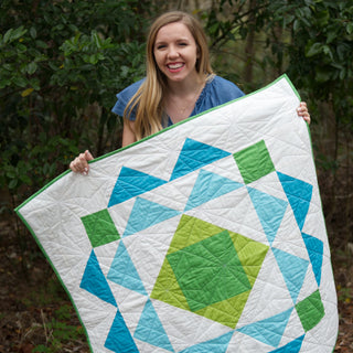 Homemade Emily Jane Paradigm Quilt Pattern (Download) featuring a bold geometric quilt with turquoise green and white angular shapes held by a smiling woman outdoors