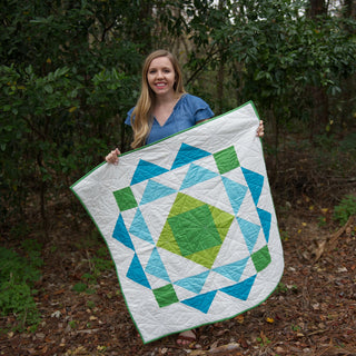 Homemade Emily Jane Paradigm Quilt Pattern (Download) shown as a modern geometric quilt with blue green and white shapes held outdoors by a smiling maker