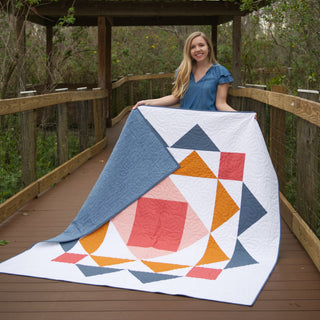 Paradigm Quilt Pattern (Download) by Homemade Emily Jane featuring a modern geometric quilt in blue, coral, orange, and white tones held outdoors