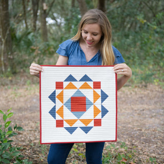 Homemade Emily Jane holds a modern geometric quilt with blue orange and red shapes in a woodland setting Paradigm Quilt Pattern (Download)
