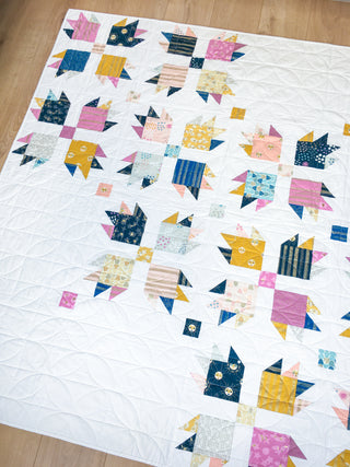 Close-up of a colorful quilt featuring geometric blocks with paw print shapes on a white background, created using the Paw Tracks Quilt Pattern (Download) by Lou Orth Designs.