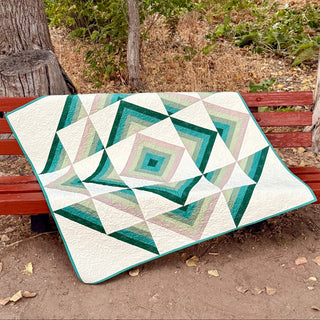 Modern geometric quilt with teal, green, and cream tones displayed on a red bench outdoors, showcasing the Percussion Quilt Pattern (Download) by Shadow Valley Quilts.
