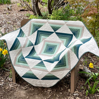 A neatly displayed quilt featuring a geometric pattern in soothing green, blue, and neutral tones, showcasing the Percussion Quilt Pattern (Download) by Shadow Valley Quilts.