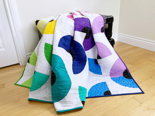 Colorful geometric quilt with curved piecing in bright blues, purples, greens, and yellows, showcasing the Pie in the Sky Quilt Pattern (Download) by Penny Spool Quilts.
