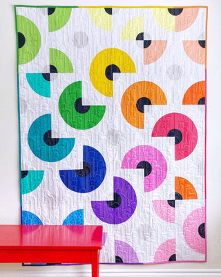 Colorful modern quilt with curved geometric shapes in various bright hues on white background, showcasing Pie in the Sky Quilt Pattern (Download) by Penny Spool Quilts.