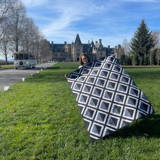 Person holding a black and white geometric quilt made with the Pine Shadow Quilt Pattern (Download) by Hampton Quilt Studio, standing on a green lawn with a historic mansion in the background.