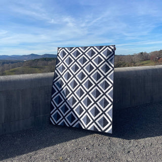 Modern geometric black and white quilt displayed outdoors with rolling hills in background, showcasing the Pine Shadow Quilt Pattern (Download) from Hampton Quilt Studio.
