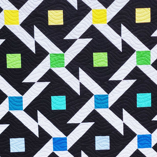 Pivoting Quilt Pattern by Staci W Quilts closeup: black background with white geometric arrows and colorful squares in yellow, green, teal, and blue.
