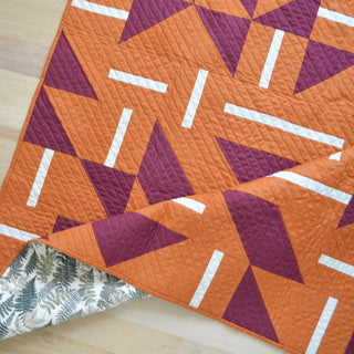 Close-up of a modern quilt in burnt orange and maroon with geometric shapes and white accents, showing detailed stitching, made using the Playroom Quilt Pattern (Download) by Sewn.