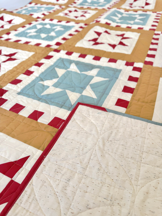 Postmark Quilt Pattern by Sew & Sew Quilting Co. closeup: 4-tone colorway with light blue, red, tan, and cream geometric star blocks with red sashing.
