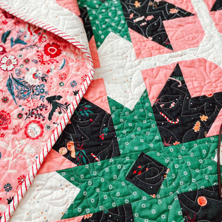 Present Parcels Quilt Pattern by A Piece of Quiet Quilts closeup: star block detail with pink floral, dark green, and black novelty print fabrics and swirl quilting.