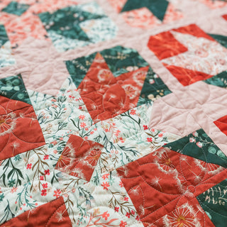 Close-up of a colorful quilt with red, green, and floral patterns showcasing the Present Parcels Quilt Pattern (Download) by A Piece of Quiet Quilts, perfect for confident beginners.