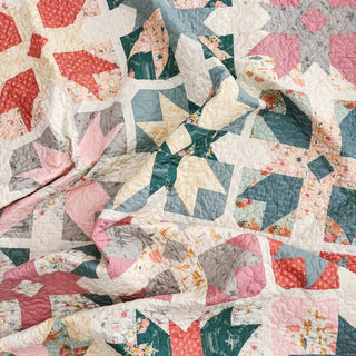 Close-up of a colorful quilt with star and geometric patterns in soft pink, green, red, and cream tones, showcasing intricate stitching and design from A Piece of Quiet Quilts using Present Parcels Quilt Pattern (Download).