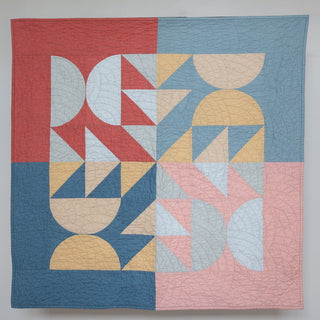Modern geometric quilt in soft red, blue, beige, and pink tones showcasing the Relative Time Quilt Pattern (Download) by Wood Lily Studio with HST and flying geese designs.