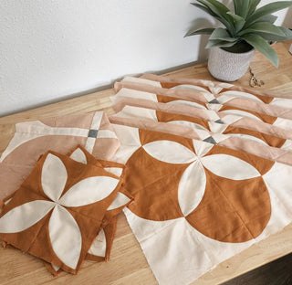 Quilt with geometric pattern on a wooden surface with a plant in the background
