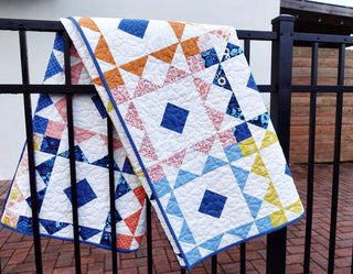 Reverberate Quilt Pattern (Download) by Homemade Emily Jane featuring colorful geometric quilts in blue white orange pink and yellow draped over a railing