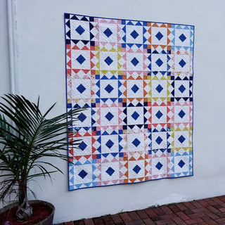 Reverberate Quilt Pattern (Download) by Homemade Emily Jane, a colorful modern geometric quilt with repeating diamond and triangle blocks displayed on a wall