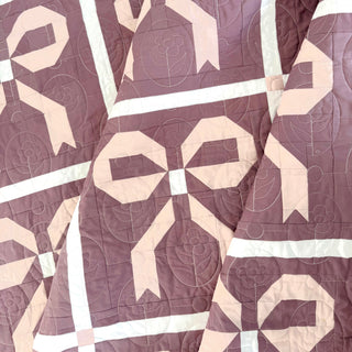 Close-up of a mauve and pink quilt with bow shapes and floral quilting, showcasing the Ribbons & Bows Quilt Pattern (Download) by Sew & Sew Quilting Co.
