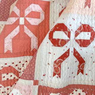 Ribbons & Bows Quilt Pattern by Sew & Sew Quilting Co. closeup: multiple bow blocks in shades of coral pink, red, and white with various patterned fabrics.