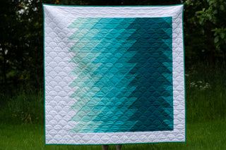 A modern quilt featuring a gradient ripple design in shades of teal and aqua against a white background, showcasing the Ripple Quilt Pattern (Download) by Lou Orth Designs.