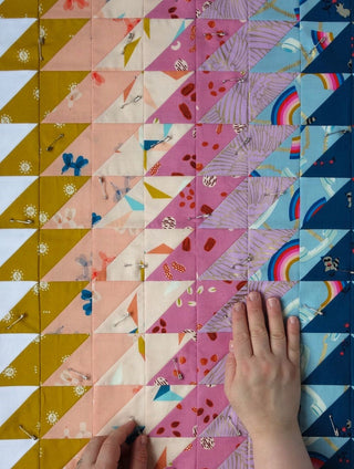 Closeup of colorful quilt blocks pinned and arranged in a geometric Ripple Quilt Pattern (Download) by Lou Orth Designs, showing hands adjusting fabric pieces.