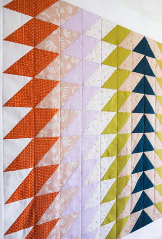 Close-up of a colorful quilt made with the Ripple Quilt Pattern (Download) by Lou Orth Designs, showcasing a geometric design with orange, purple, green, and blue fabric triangles.