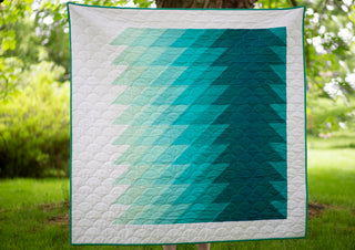 Ripple quilt by Lou Orth Designs with a gradient green pattern displayed outdoors on grass