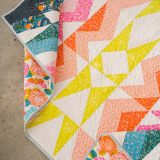 Colorful geometric quilt with orange, pink, yellow, and teal fabric patterns showcasing the Rocky Coast Quilt Pattern (Download) by Toad & Sew in a bright, modern design.