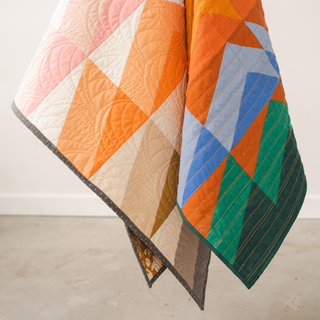 Closeup of a colorful geometric quilt featuring orange, blue, green, and neutral tones made using the Rocky Coast Quilt Pattern (Download) by Toad & Sew.