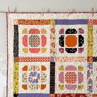 Close-up of a colorful handmade quilt featuring floral and geometric patterns, showcasing the Saltbox Quilt Pattern (Download) by The Dandy Patch.