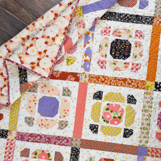 Close-up of a floral and geometric modern quilt made using the Saltbox Quilt Pattern (Download) by The Dandy Patch, featuring colorful fabric blocks and intricate stitching.