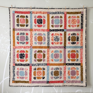Colorful handmade quilt with geometric floral blocks in warm and cool tones, showcasing the Saltbox Quilt Pattern (Download) by The Dandy Patch.