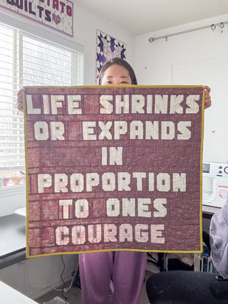 Person holding a quilted fabric piece with bold white letters on a purple background reading an inspirational quote, made using the Say Something Bold Alphabet FPP Pattern (Download) by Sweet Potato Quilts.