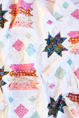 Close-up of a colorful quilt featuring vibrant star and geometric shapes with patterned fabrics by Lou Orth Designs, showcasing the Shooting Stars Quilt Pattern (Download).