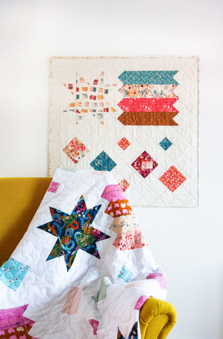 Quilt and wall hanging featuring star and geometric block designs in vibrant fabrics on white background, showcasing Shooting Stars Quilt Pattern (Download) by Lou Orth Designs.