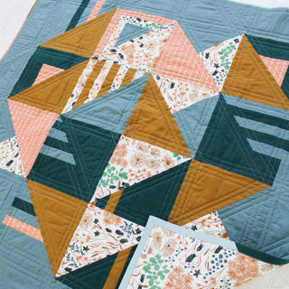 Close-up of a quilt featuring blues, mustard, pink, and floral fabrics with geometric stitching, made using the Sincerely Quilt Pattern (Download) by Eudaimonia Studio.