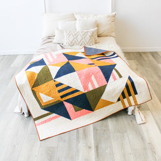 Colorful modern geometric quilt draped on a bed, featuring blue, pink, mustard, and olive tones, showcasing the Sincerely Quilt Pattern (Download) by Eudaimonia Studio.
